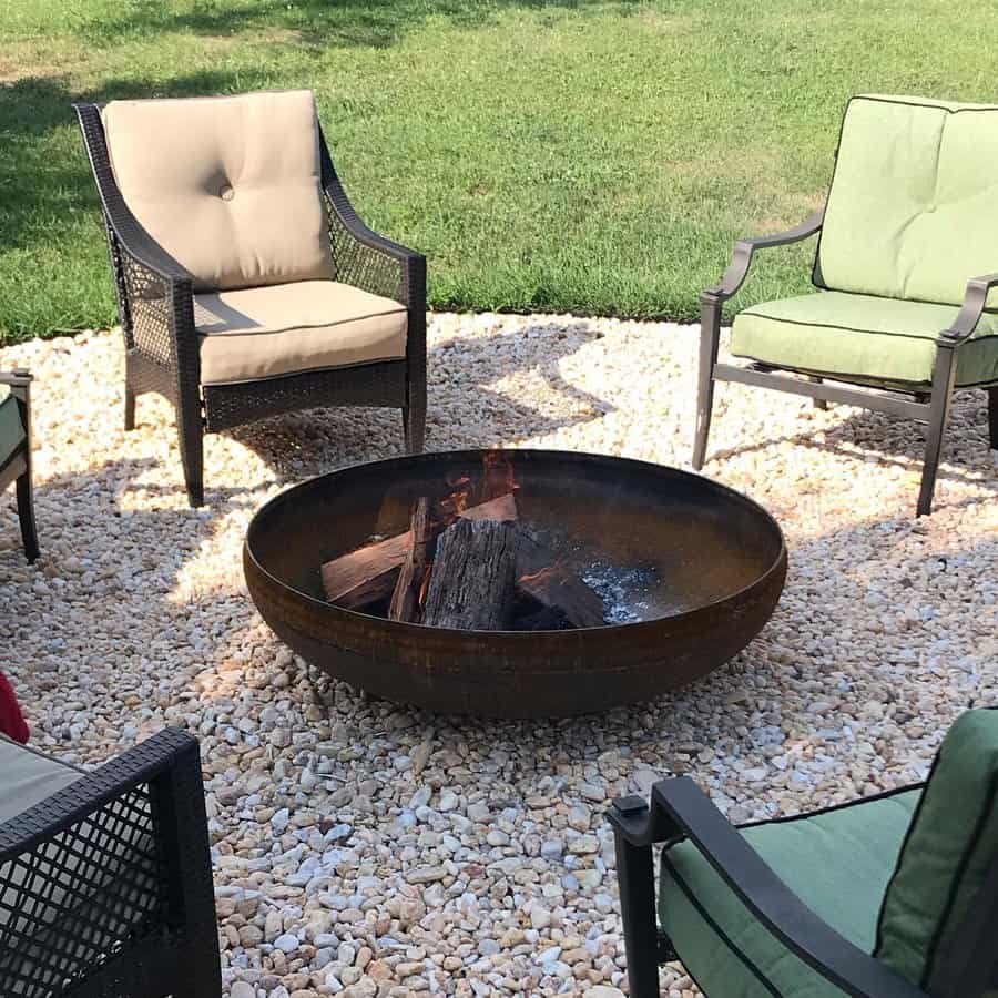 Fire pit on gravel patio surrounded by cushioned chairs on a sunny day