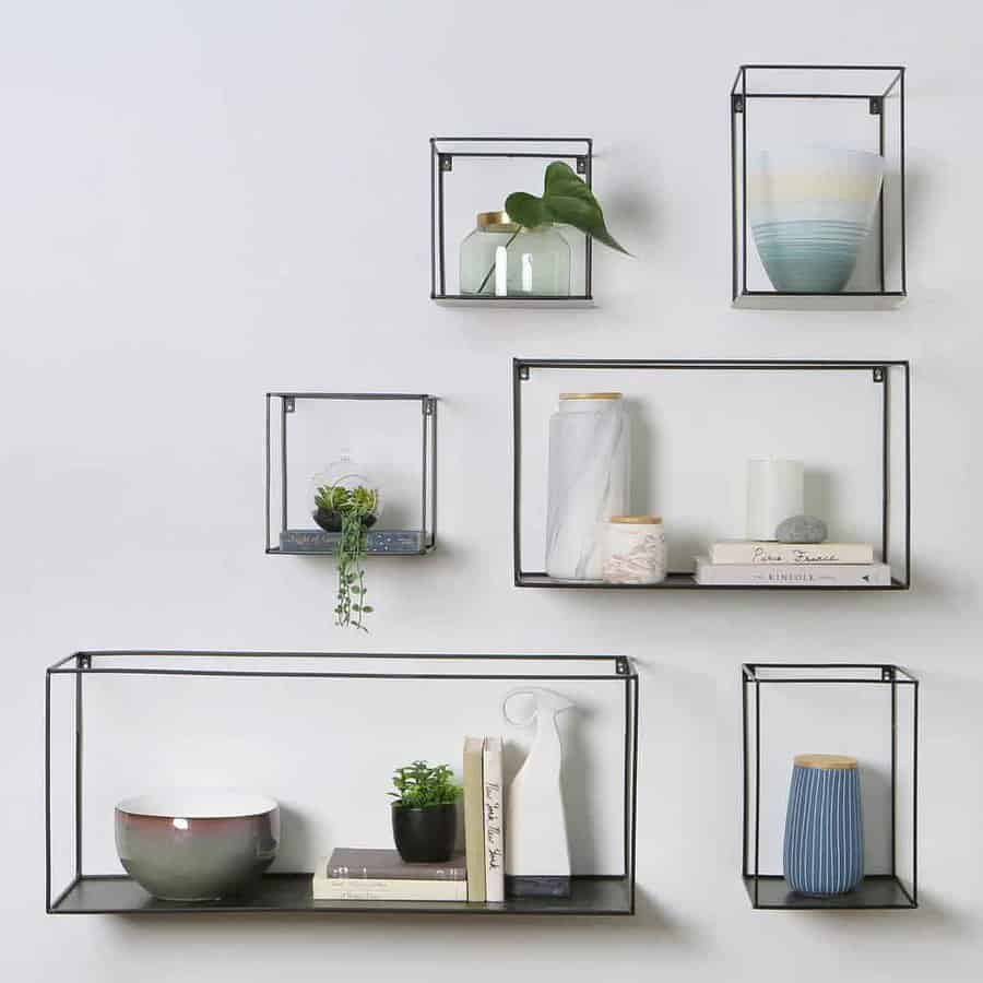 Modern black metal floating shelves in geometric shapes, decorated with books, vases, and plants for a minimalist wall display