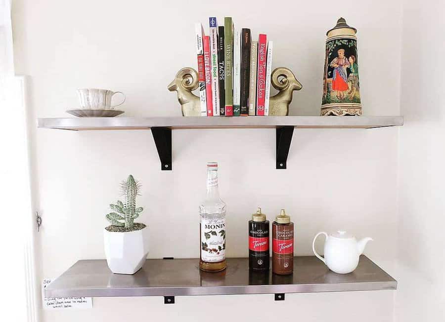 Two wall shelves with a teacup, books, decorative items, bottles, a cactus, and a teapot arranged neatly against a white background