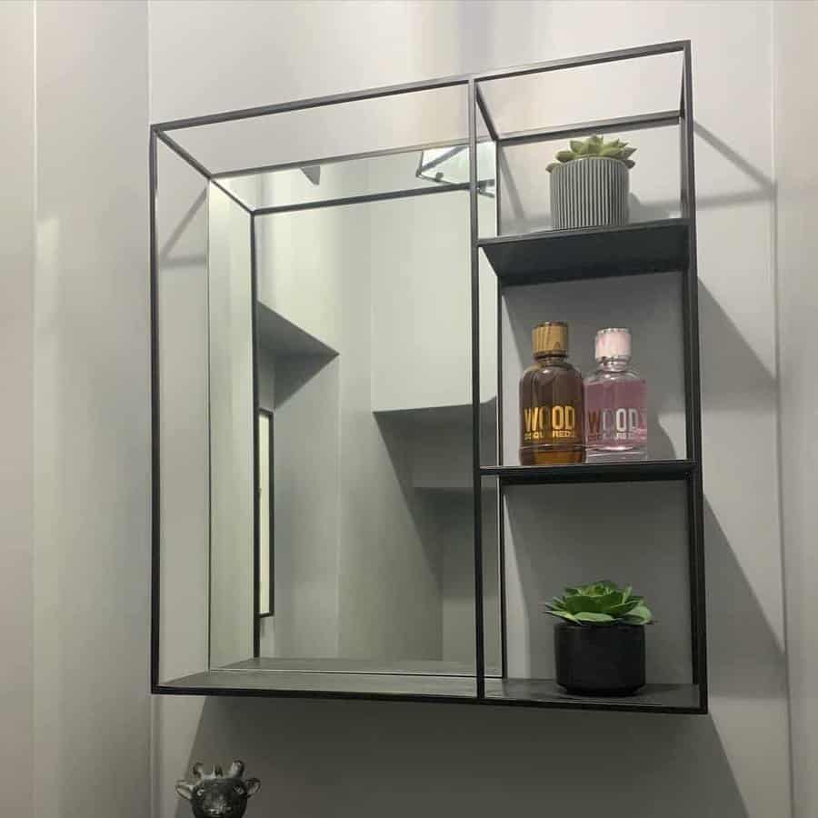 Modern black metal floating shelf with a mirror, holding perfume bottles and small potted plants for a sleek and minimalist look