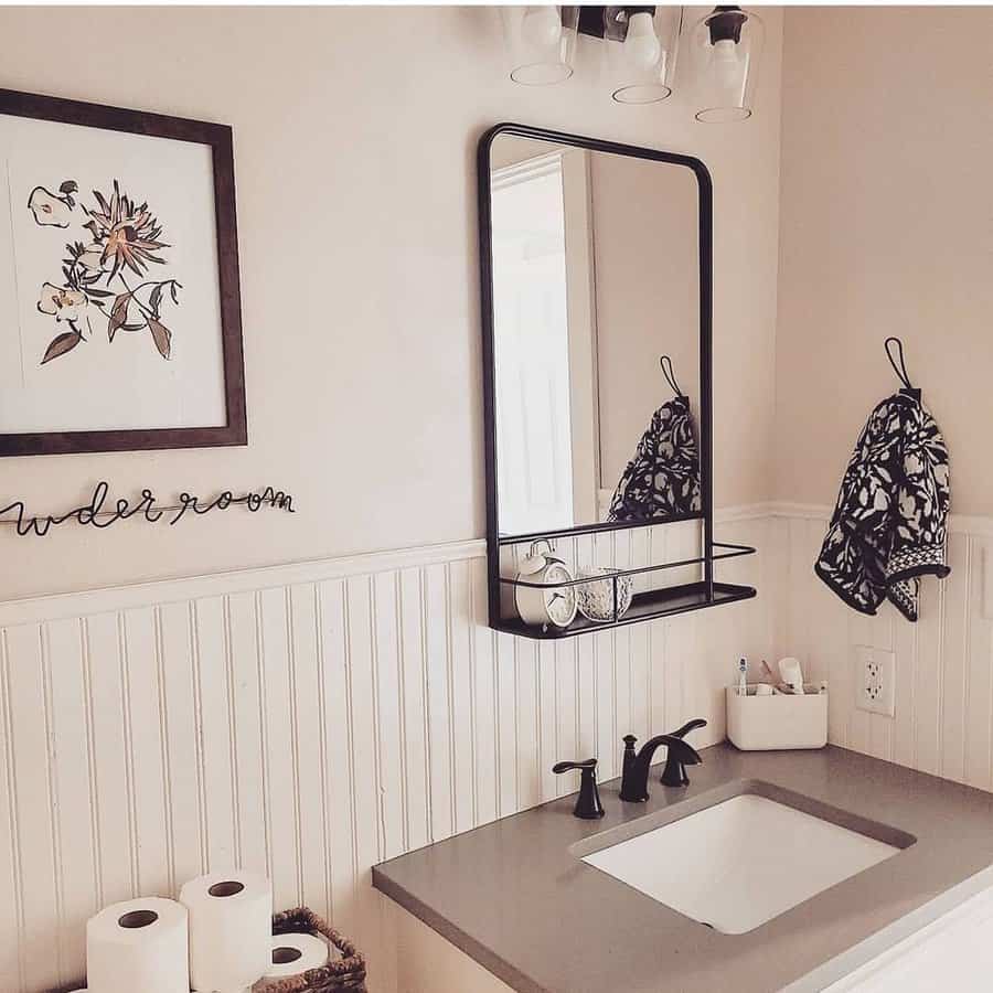 A bathroom interior with a framed floral picture, a rectangular mirror, a faucet sink, folded towels, a soap dispenser, and toilet paper