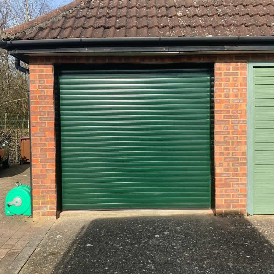 Green roller garage door on a brick building with tiled roof