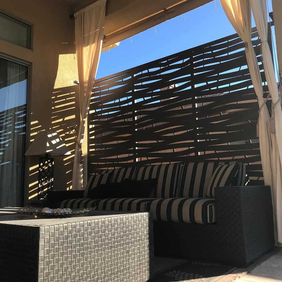 Modern patio with a decorative metal privacy screen, sheer curtains, striped cushioned seating, and woven furniture for a cozy shaded retreat