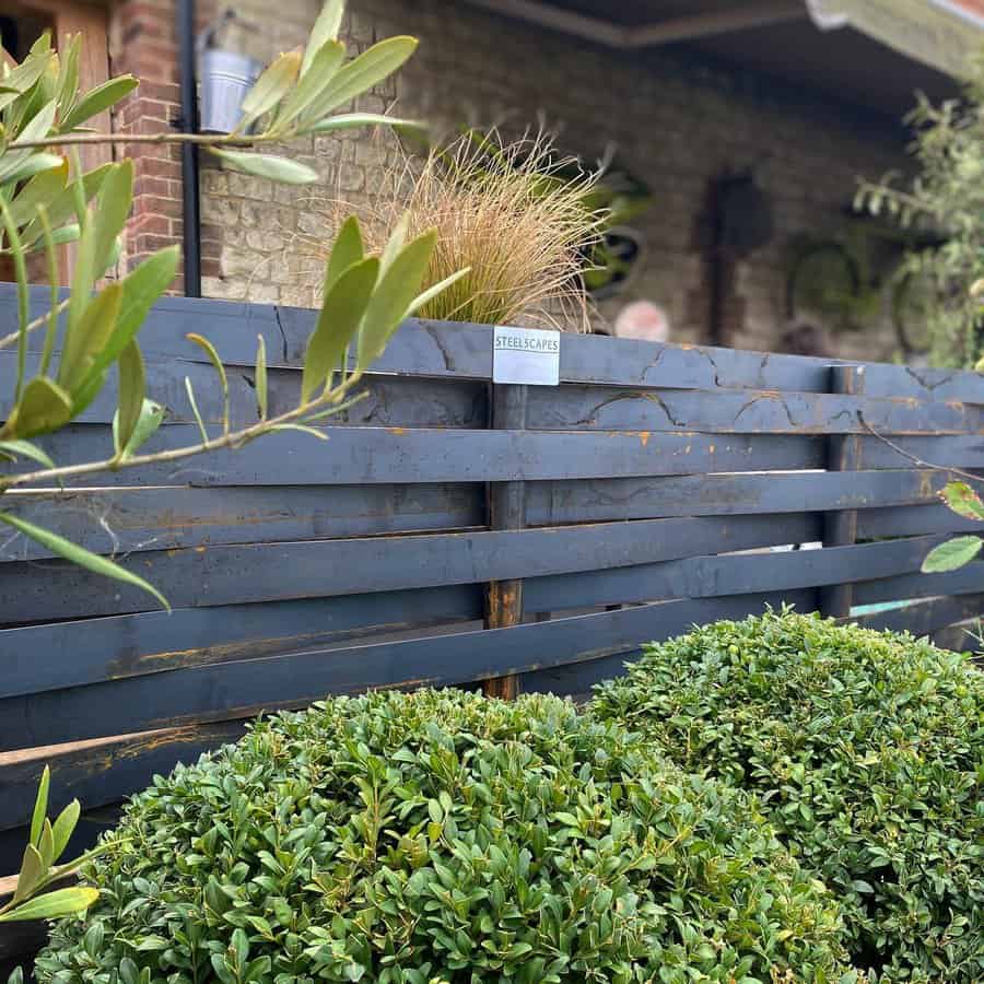 Dark slatted metal fence with greenery