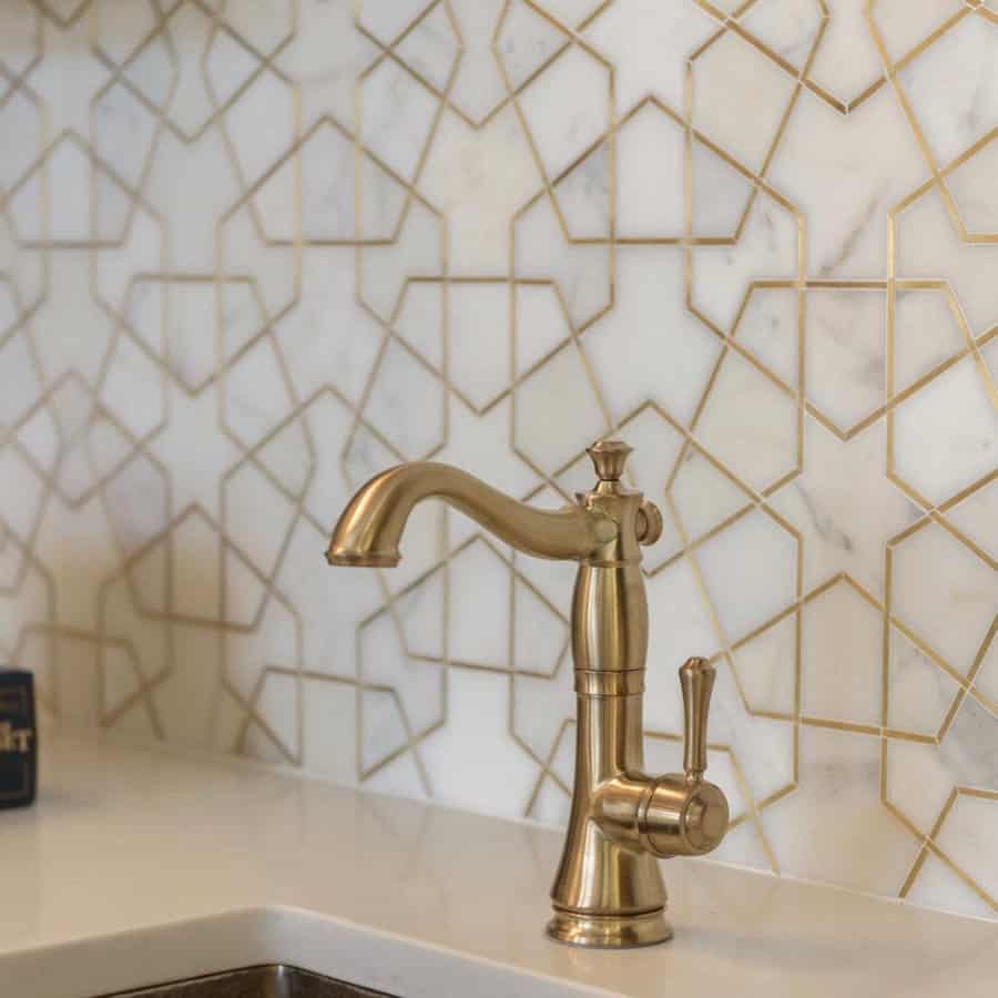 Elegant bathroom with white marble backsplash featuring gold geometric inlays and a vintage-style brushed gold faucet.