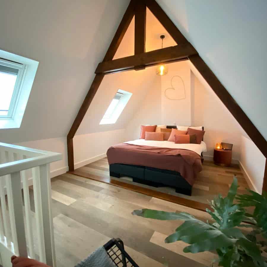 Minimalist attic bedroom with exposed wooden beams, warm lighting, and earthy-toned bedding. Skylights bring in natural light for a cozy retreat.