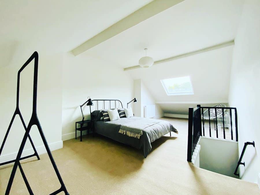 Minimalist attic bedroom with a sleek black metal bed frame, neutral tones, and skylights. Clean lines and open space create a modern retreat.