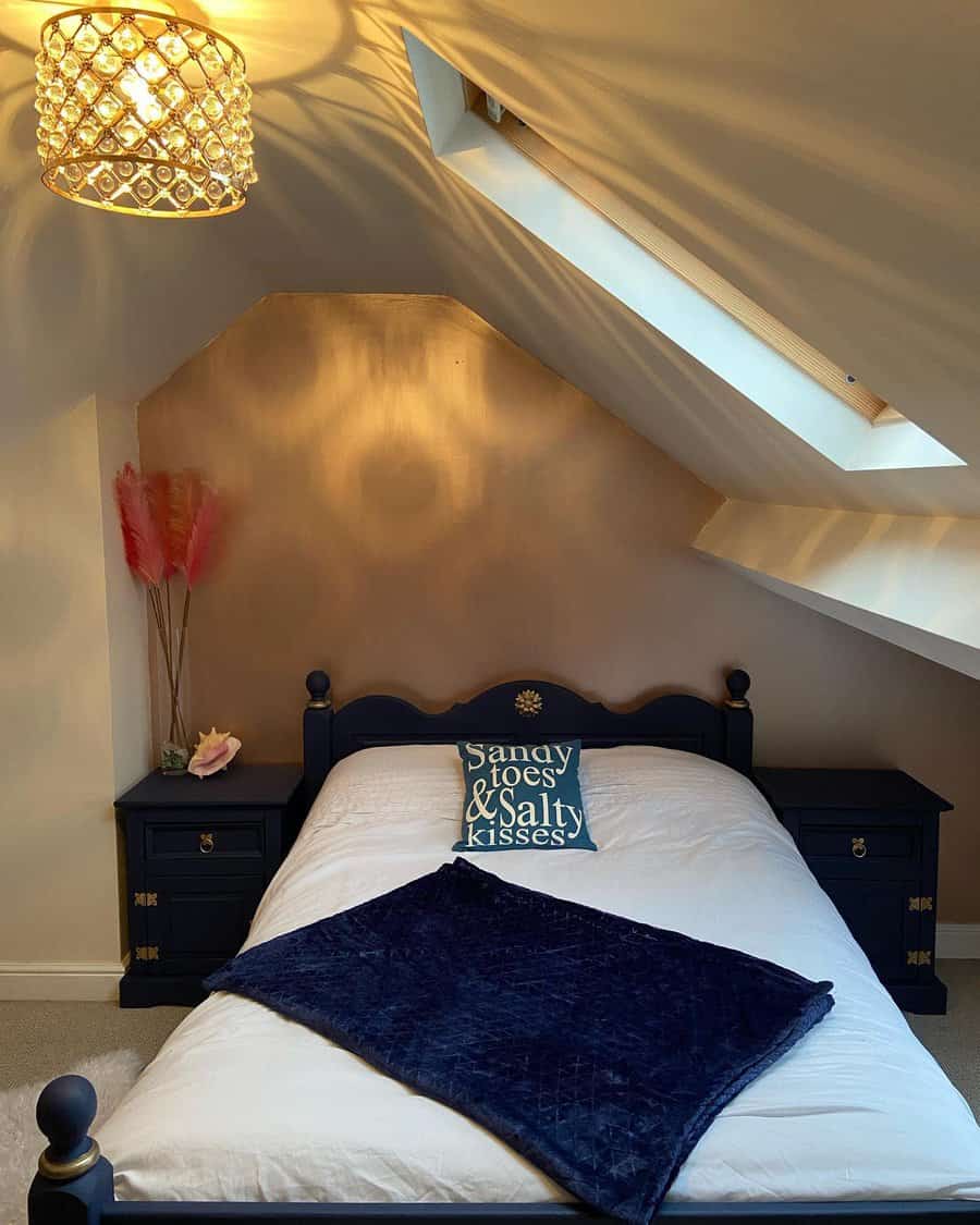 Cozy attic bedroom with a navy blue bed frame, warm lighting, and a skylight. Gold accents and soft textures create a charming, intimate retreat.