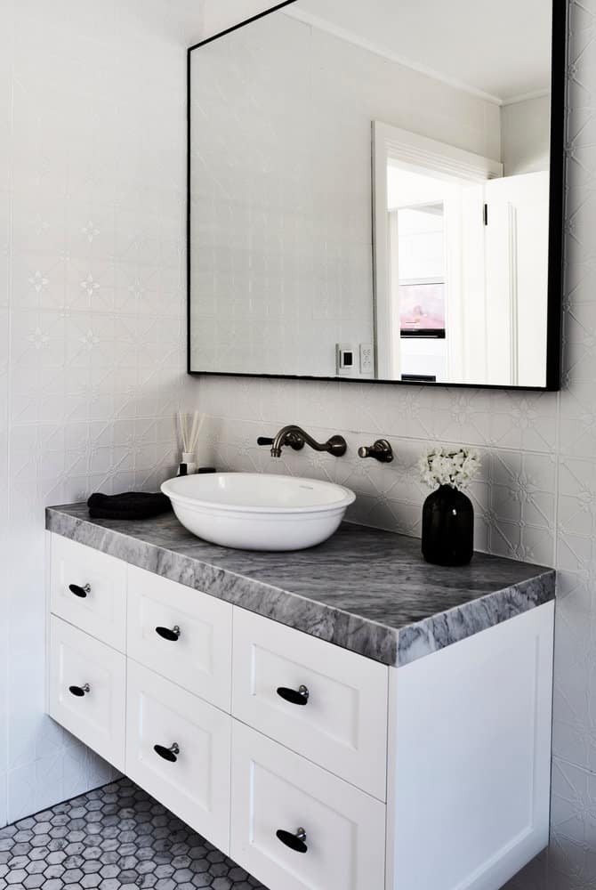 Modern bathroom with a marble countertop, round basin, large mirror, and white cabinets featuring hexagonal mosaic floor tiles