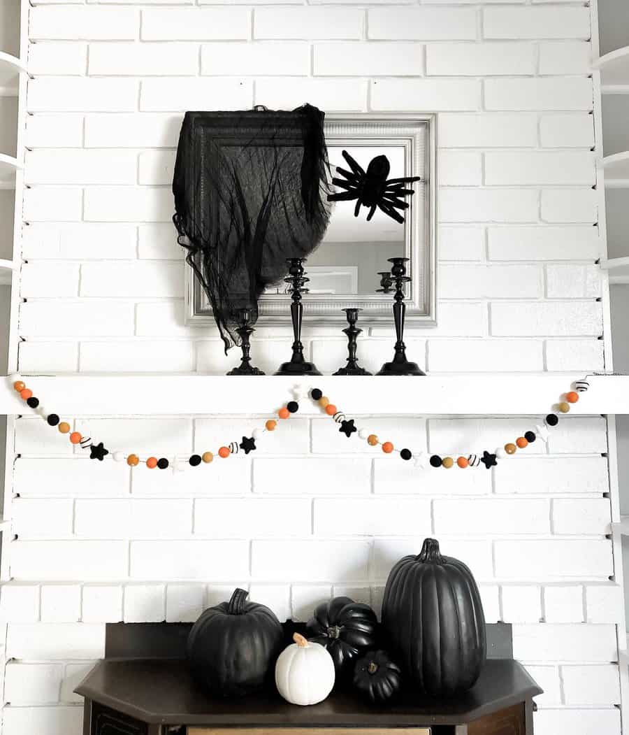 Halloween decor with black pumpkins, a spider, candlesticks, and an orange garland