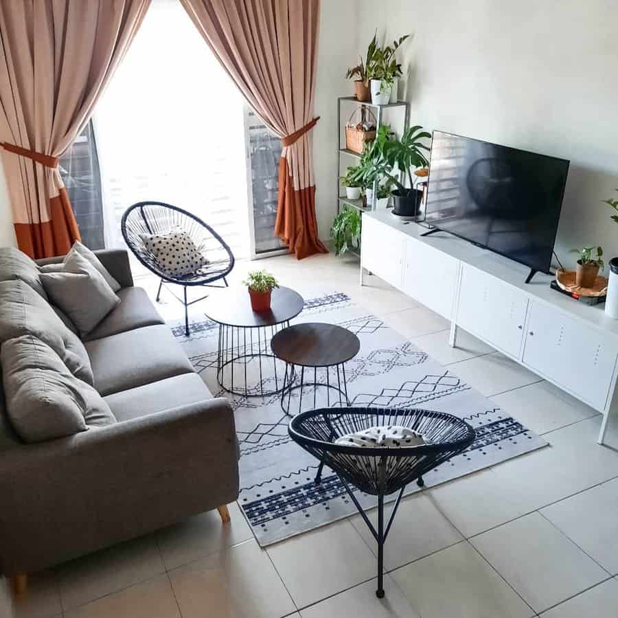 Modern living room with a sofa, chairs, TV, plants, and a rug on a tile floor