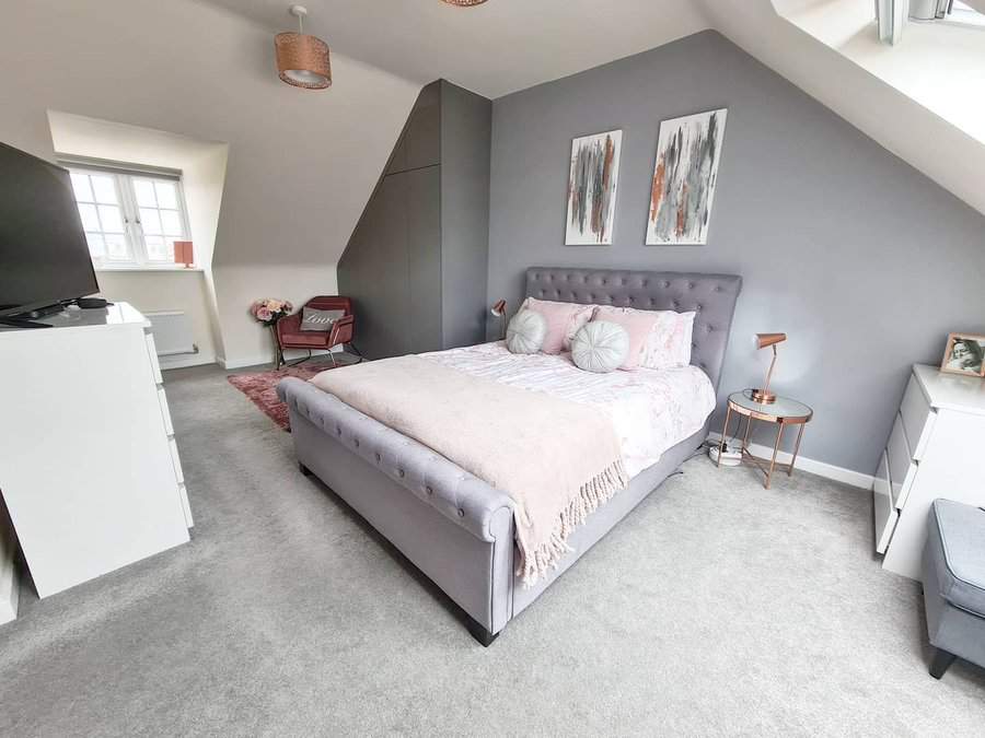 Bedroom with a gray upholstered bed, two abstract paintings, side tables, a TV, and an armchair by the window