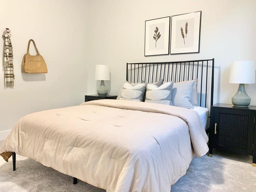 Minimalist bedroom featuring a double bed, black headboard, neutral bedding, two lamps, two framed prints, and a handbag hanging on the wall