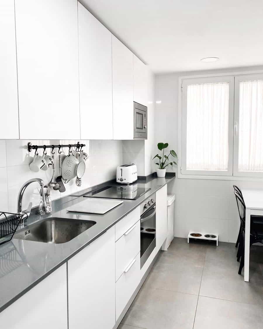 Modern white kitchen with grey countertops, plants, and ample natural light