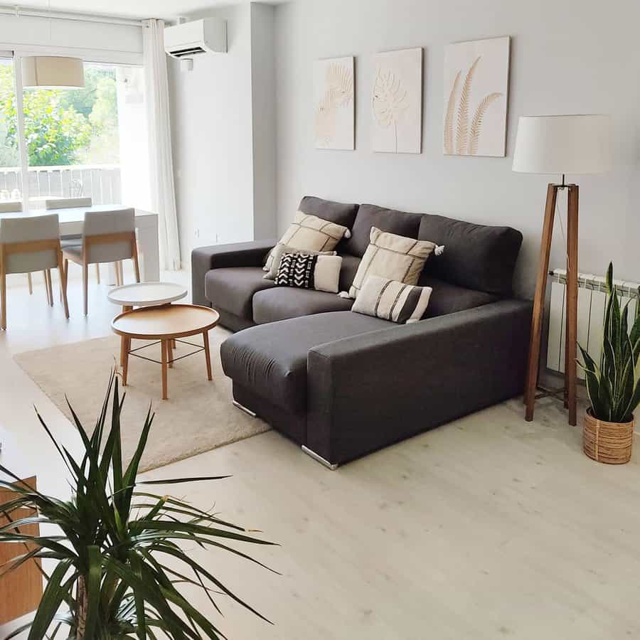 Minimalist living room with a dark gray sectional, neutral-toned pillows, wooden coffee tables, soft lighting, and greenery for a fresh, airy feel