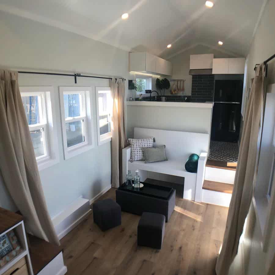 Compact minimalist living room with a built-in white bench, cozy pillows, a black accent table, and an open loft-style kitchen for a modern touch