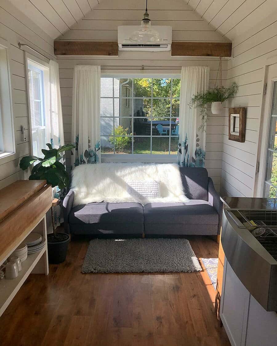 Bright tiny living room with a cozy dark gray sofa, white shiplap walls, a large window, and natural wood accents for a charming, airy feel