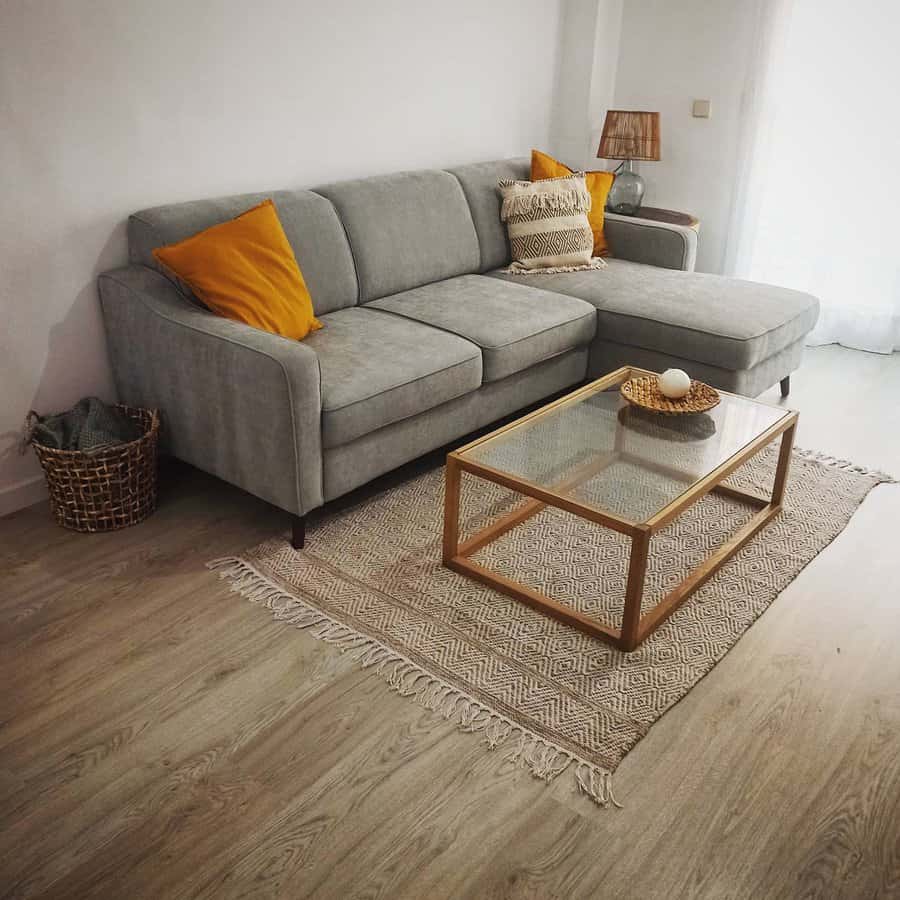 Minimalist living room with a gray sectional, mustard accent pillows, a glass-top coffee table, and a textured rug for a cozy, modern touch