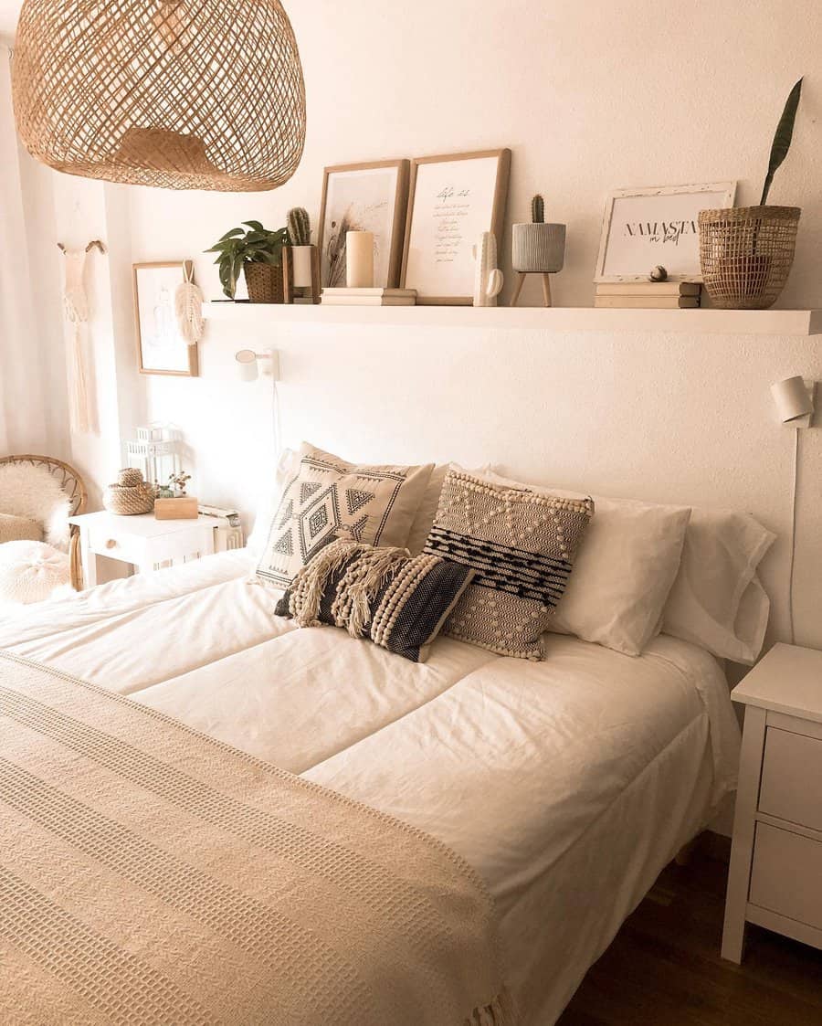 Cozy bedroom with a white bed, patterned pillows, a woven blanket, and a shelf with decor and plants above in warm, neutral tones