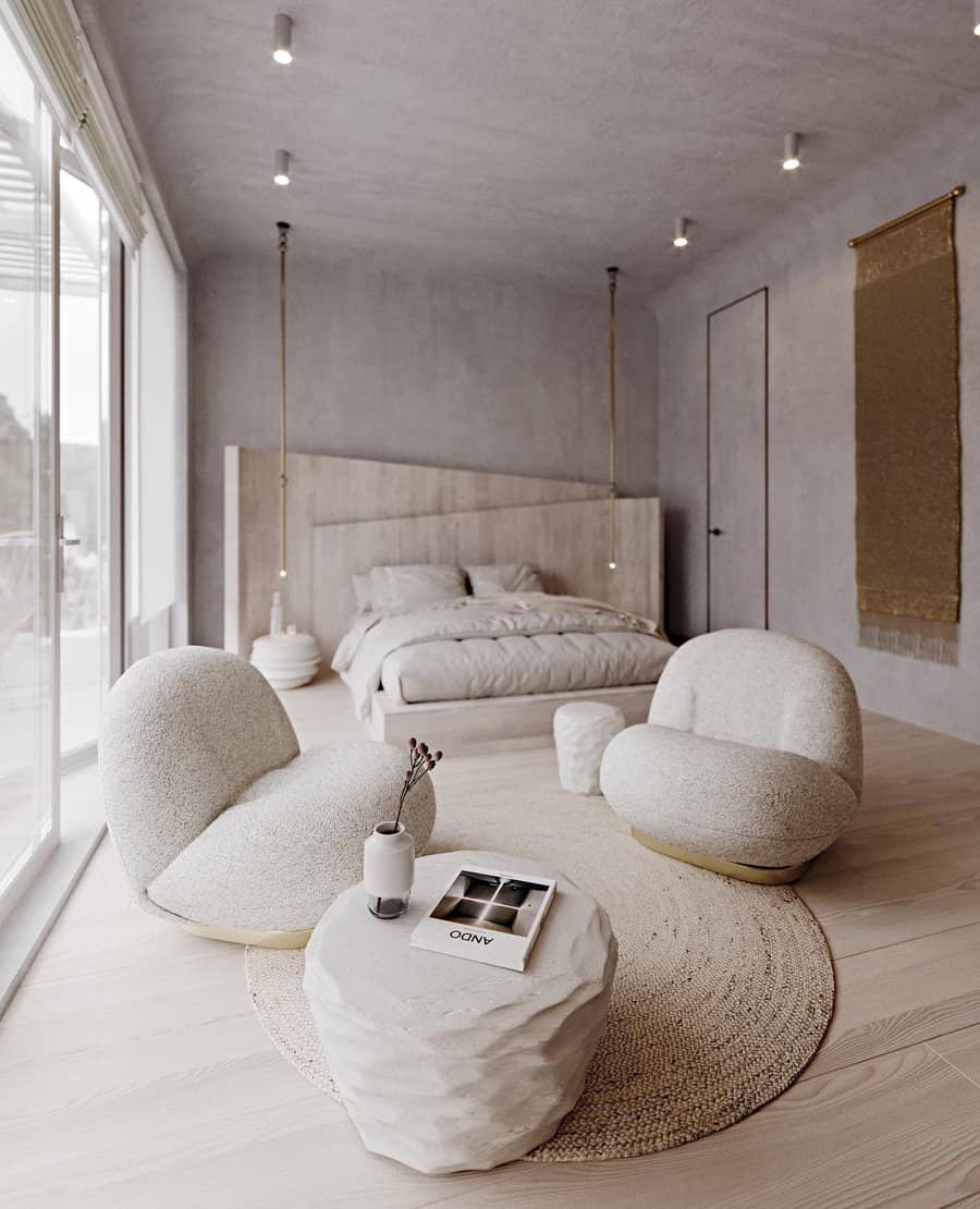 Minimalist bedroom with round chairs, a small table, and a bed; natural light streams in through large windows; neutral tones dominate