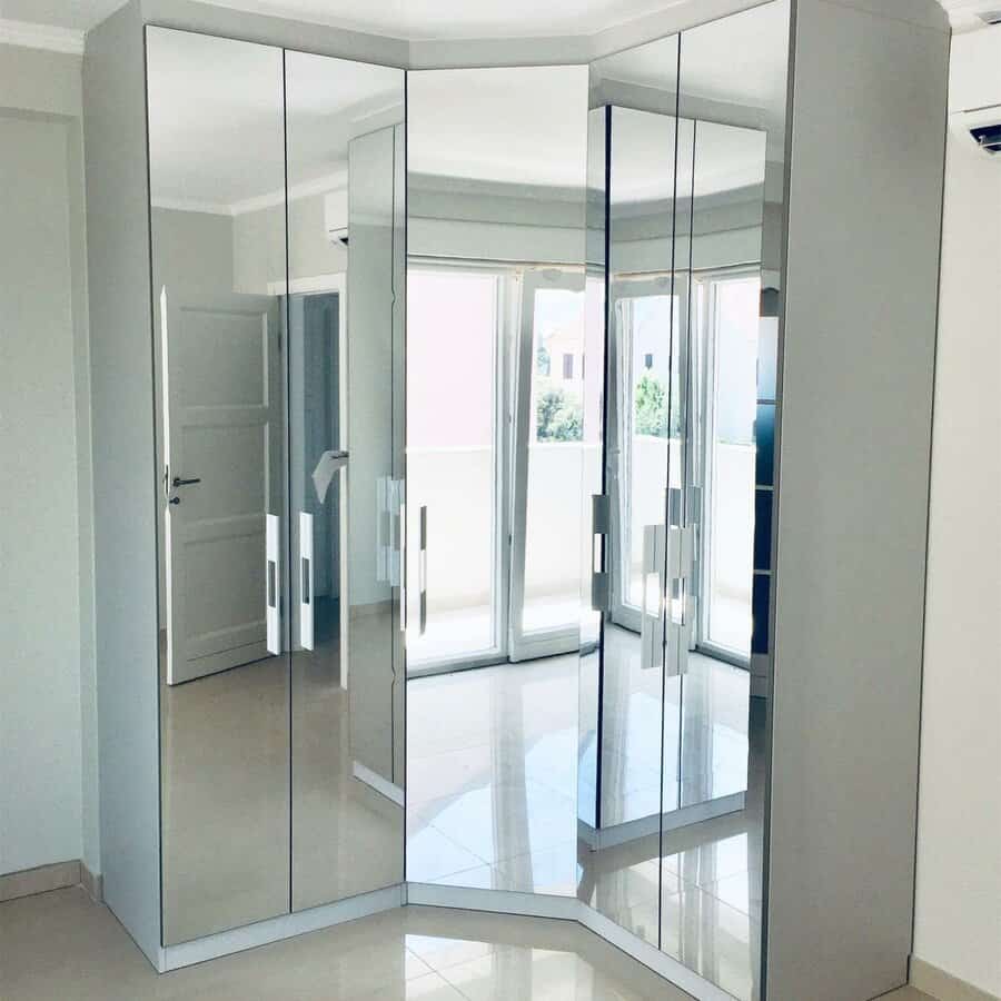 Mirrored corner wardrobe with multiple reflections, placed in a bright room with white walls and polished floor