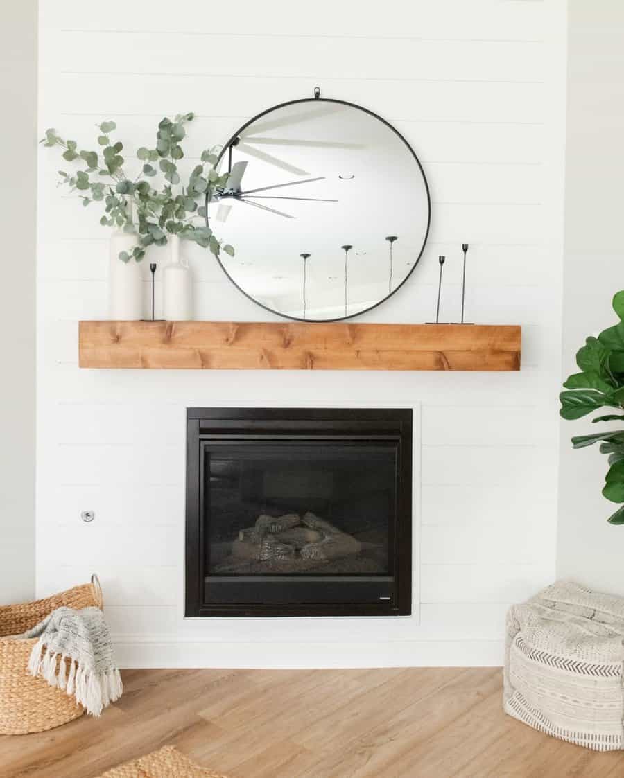 Minimalist living room with a round mirror above a wooden shelf, decorated with vases and plants, and a fireplace below