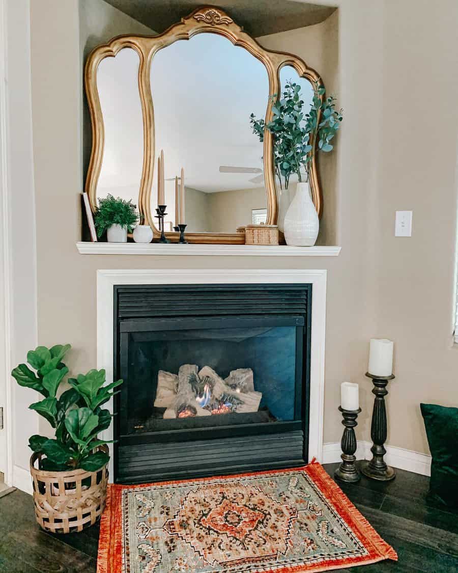 A cozy fireplace with a gold-framed mirror above, surrounded by plants, candles, and a vibrant rug, creating a warm and inviting atmosphere