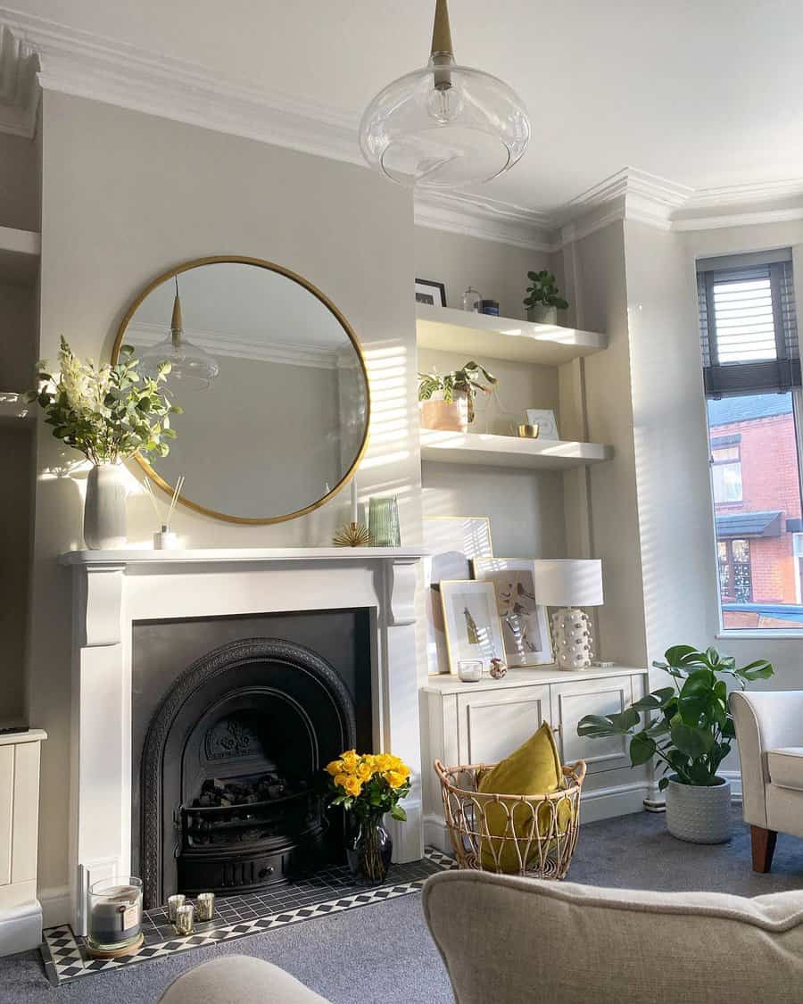 A chic white fireplace with a black insert, complemented by a round gold-framed mirror, plants, and artwork, creating a clean, modern aesthetic