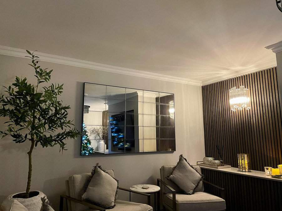 A modern living room with chairs, potted plant, mirror, and decorative lighting