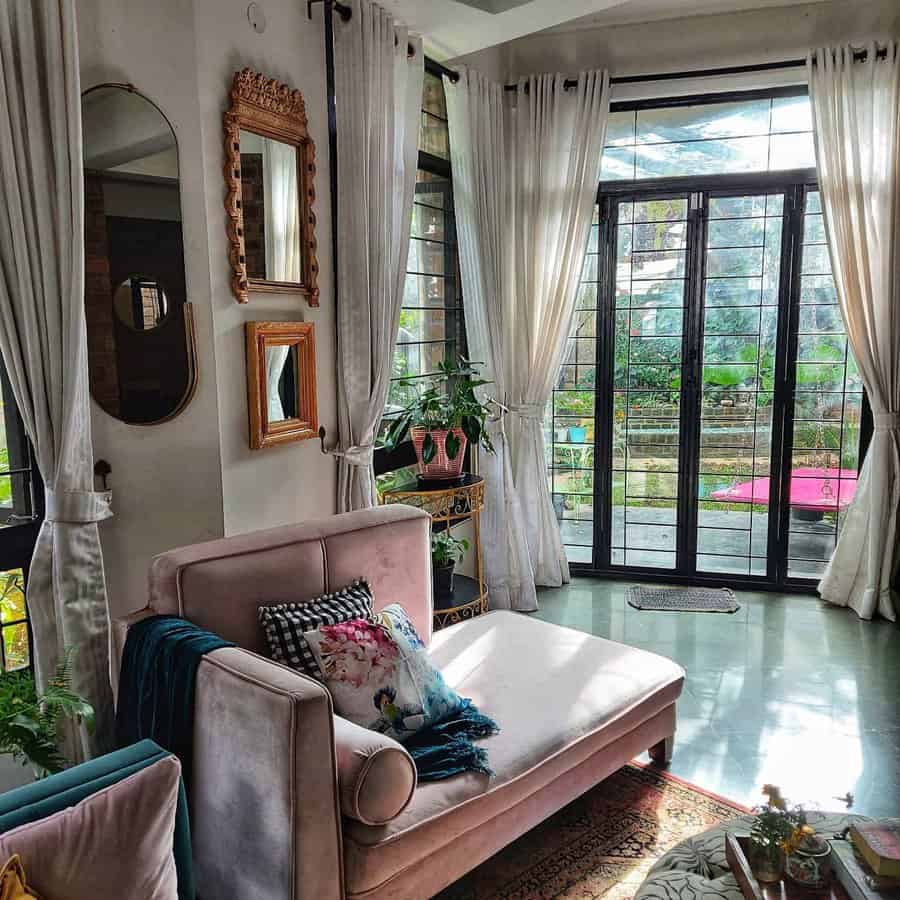 Sunlit room with a pink sofa, potted plants, mirrors, and large windows facing a garden