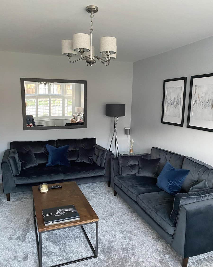 A modern living room with two dark sofas, a mirror, and framed artwork on the wall