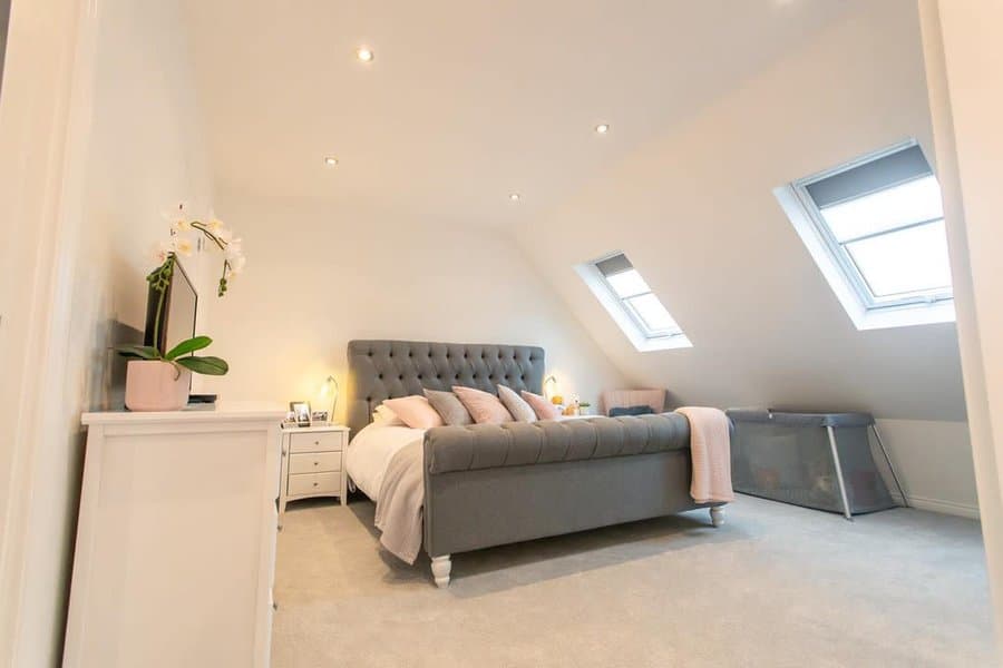 Elegant attic bedroom with a tufted gray bed, skylights, and soft neutral decor. Plush textures and natural light create a serene retreat.