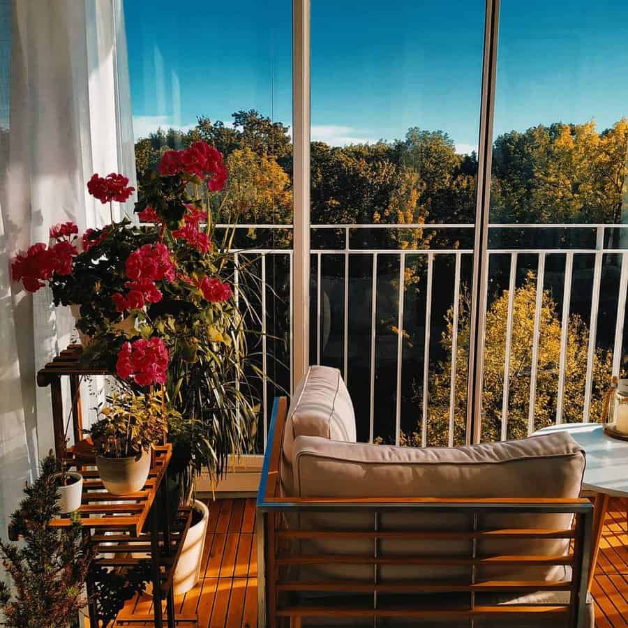 Cozy balcony with a chair, wooden floor, and potted plants, overlooking trees under a clear blue sky