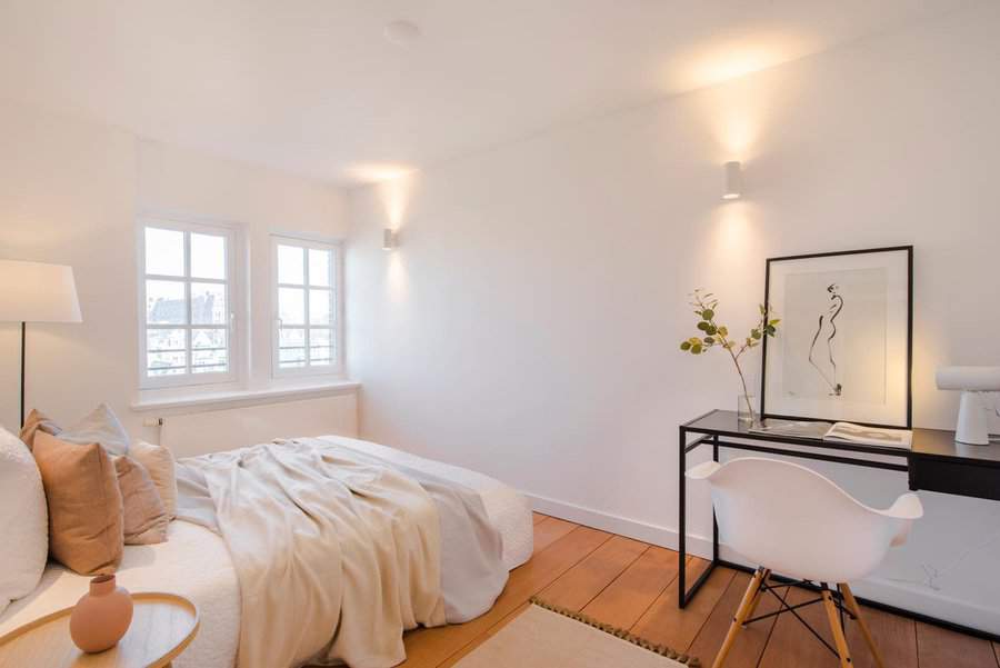 Minimalist bedroom with a cozy bed, desk with a chair, abstract artwork, and a soft glow from wall-mounted lights