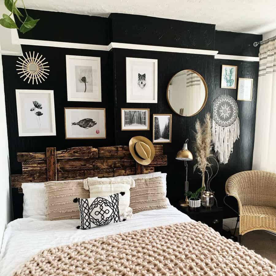 Cozy bedroom with a bohemian style, featuring a black accent wall, various framed art, a round mirror, and a wicker chair