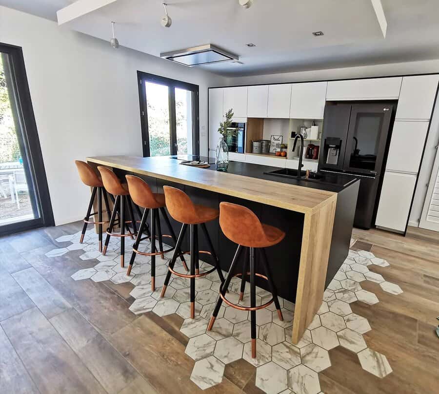 Contemporary kitchen with a black and wood waterfall breakfast bar, warm leather barstools, geometric flooring, and sleek white cabinetry