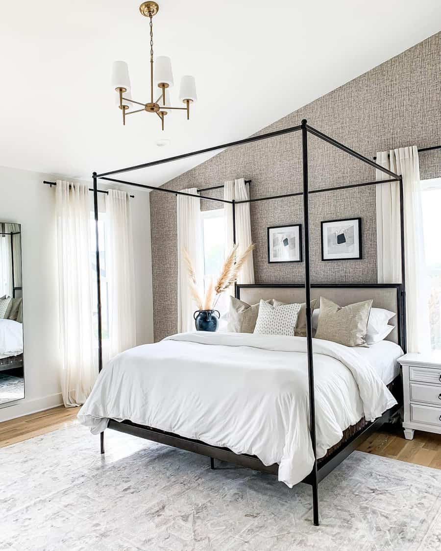 Minimalist bedroom featuring a black canopy bed, white bedding, and pampas grass in a vase with two framed pictures on a textured wall