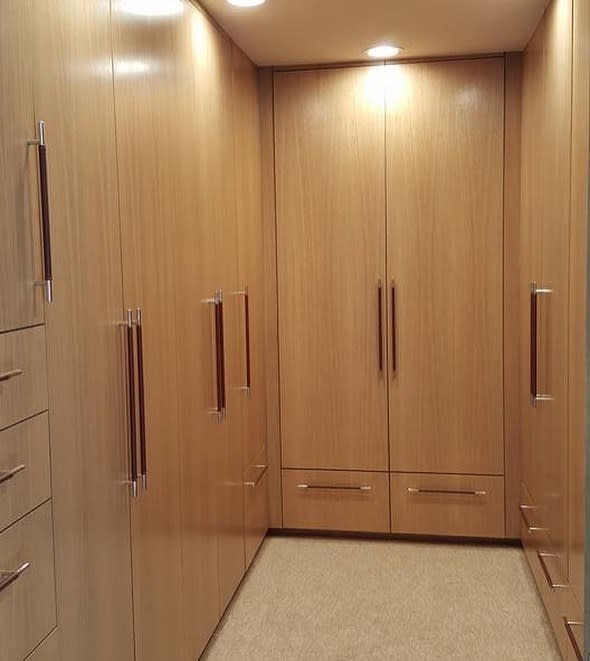 A spacious walk-in closet with light wood cabinets, brushed metal handles, and soft lighting