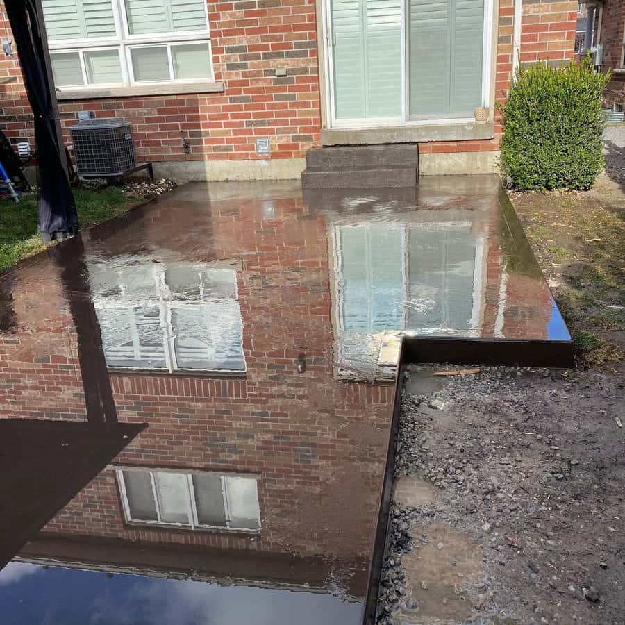 Patio with puddle reflecting brick house and windows