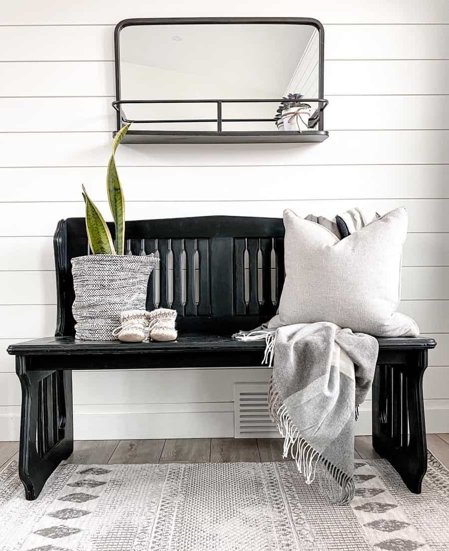 Modern farmhouse entryway with a black wooden bench, shiplap walls, cozy neutral decor, and a sleek wall mirror for a stylish, welcoming space