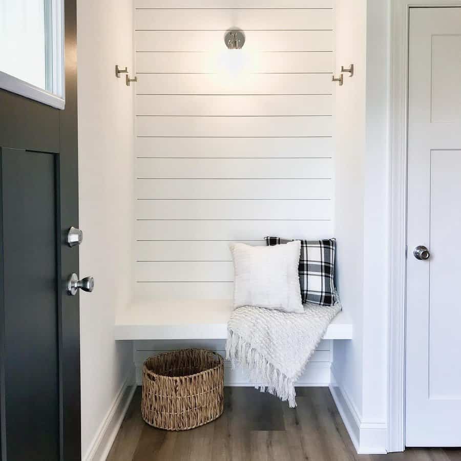 Minimalist entryway with a white bench, pillows, a throw, wicker basket, and overhead light against a shiplap wall