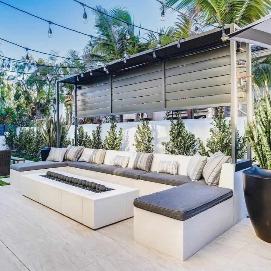 Outdoor patio with a long white sofa, gray cushions, string lights, and a modern-style fire pit