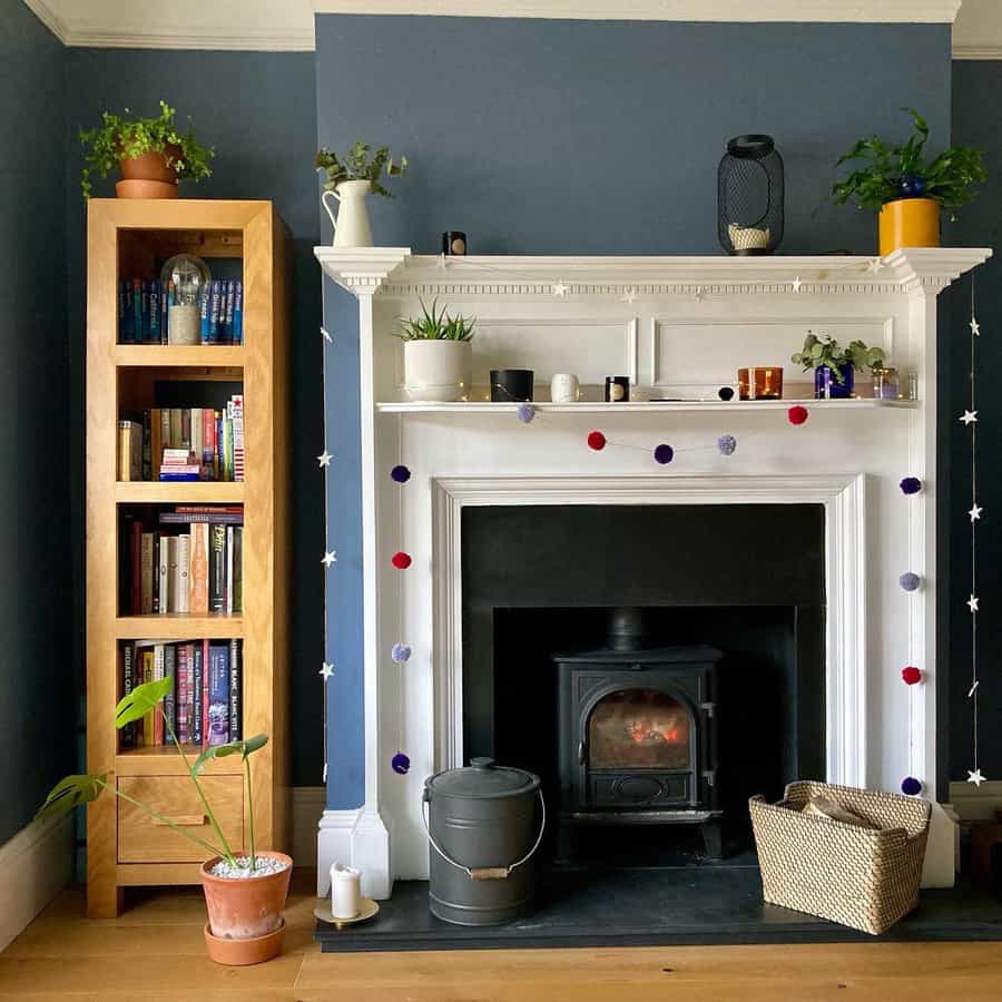 A cozy fireplace with a white mantel, decorated with candles, plants, and a colorful pom-pom garland, creating a relaxed and inviting atmosphere