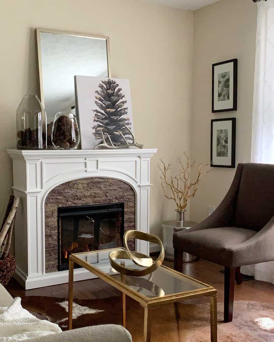 A white fireplace with a stone accent, topped with natural decor including pinecones, antlers, and a botanical print, creating a serene and stylish atmosphere