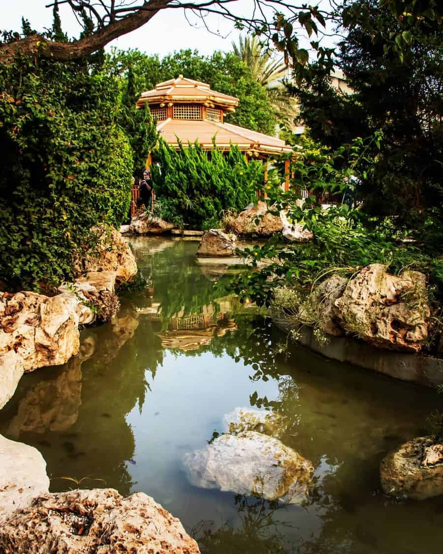 Tranquil Japanese garden with a traditional wooden pagoda, lush greenery, and a reflective pond surrounded by natural rock formations