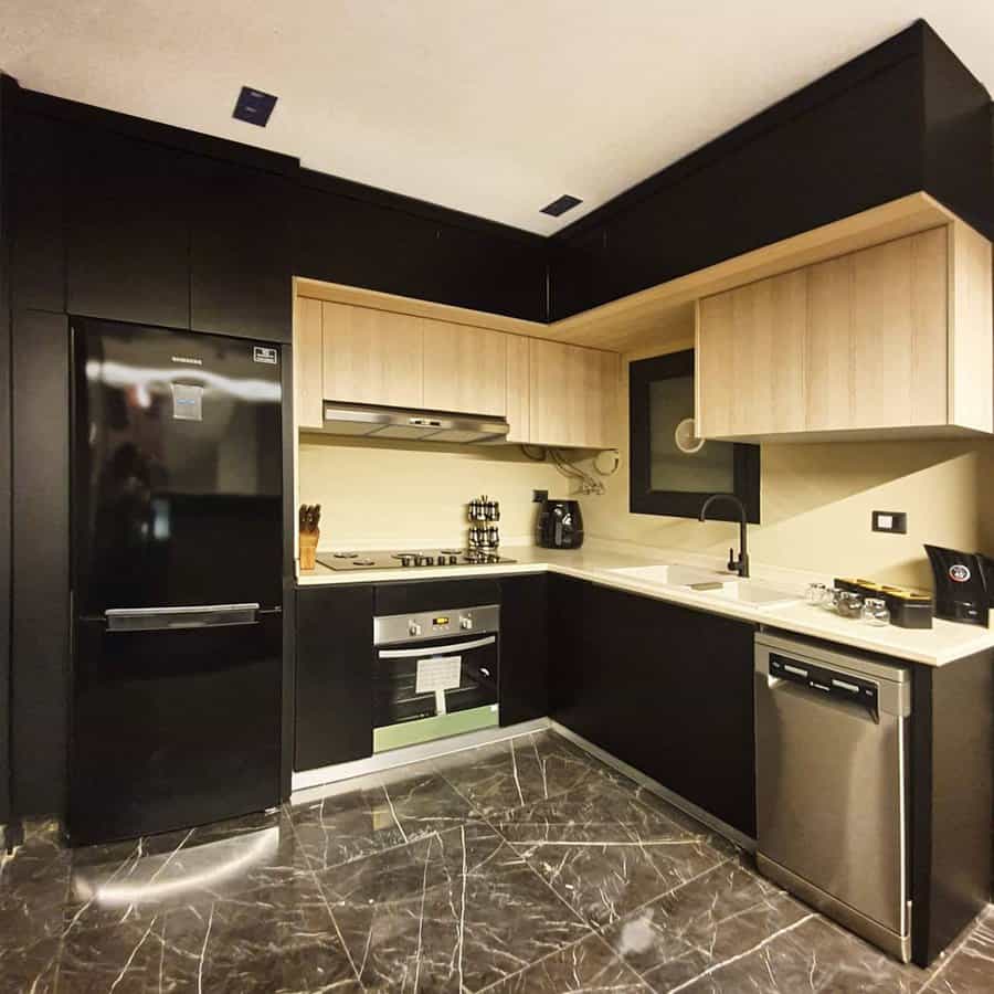 Dark marble flooring with white veining adds a luxurious touch to this modern kitchen, complementing black cabinetry and warm wood accents