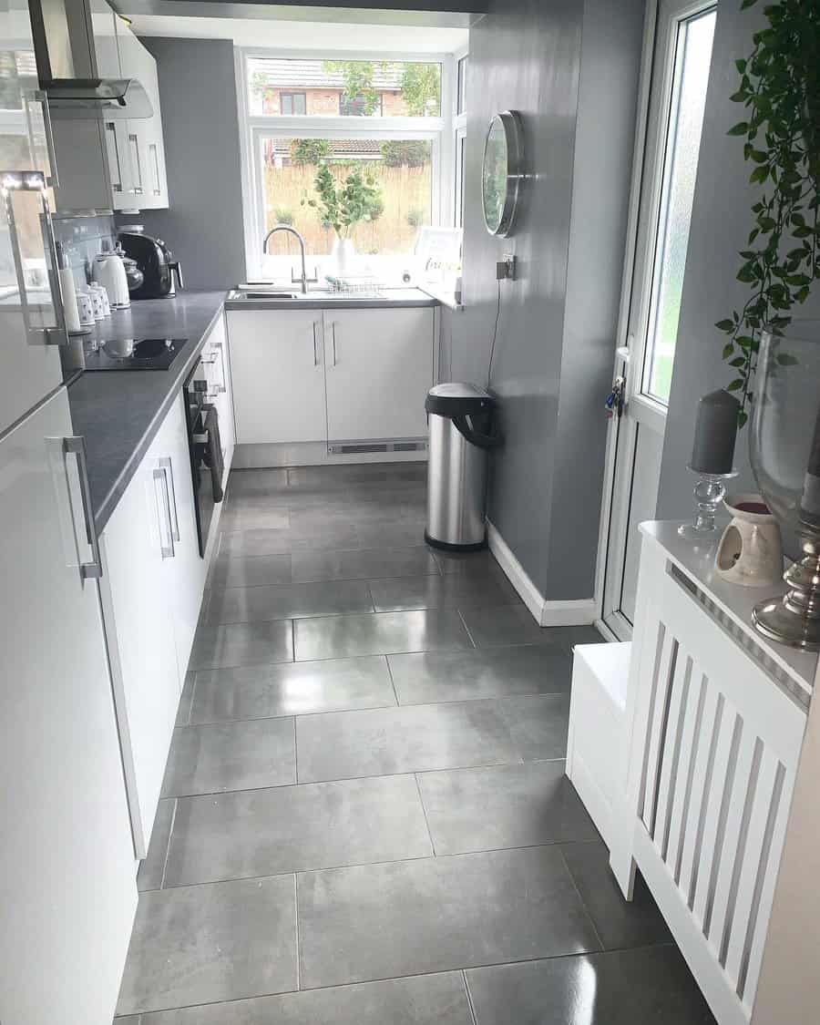 Sleek kitchen with white cabinets, gray floor tiles, stainless steel appliances, and a small round wall mirror by a large window