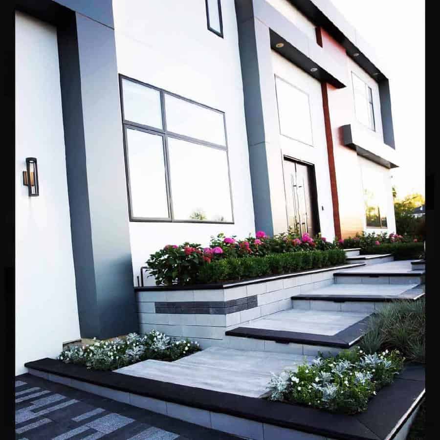 Contemporary front yard with tiered stone steps, sleek black accents, colorful flowers, and a modern facade with large windows