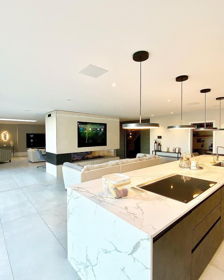 Modern open-plan living room and kitchen with marble island, couches, TV, and pendant lights featuring neutral tones and sleek design