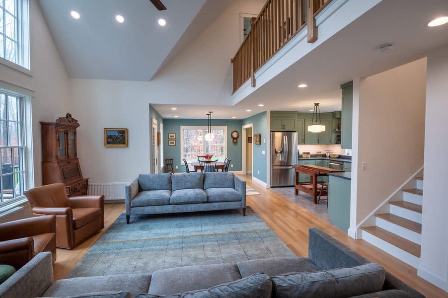 Spacious open-plan living room and kitchen with high ceilings, modern furniture, and a mezzanine where natural light streams in from large windows